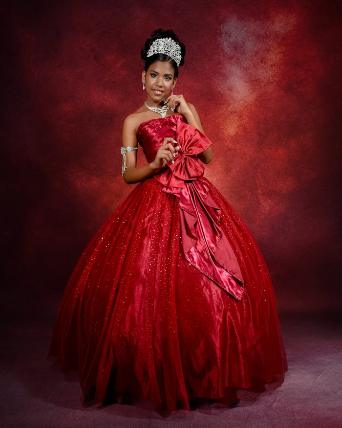 Young girl in a sparkling red quinceañera dress with elegant tiara and jewelry.